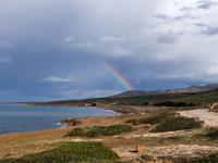 Küstenblick zu Regenbogen über den Bergen